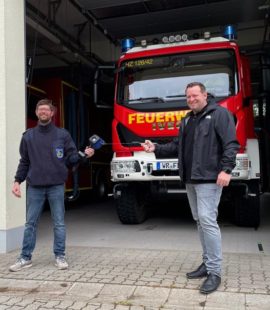 Florian Fahrtmann und Milan Fulst stehen vor einem Feuerwehrauto in der Garage