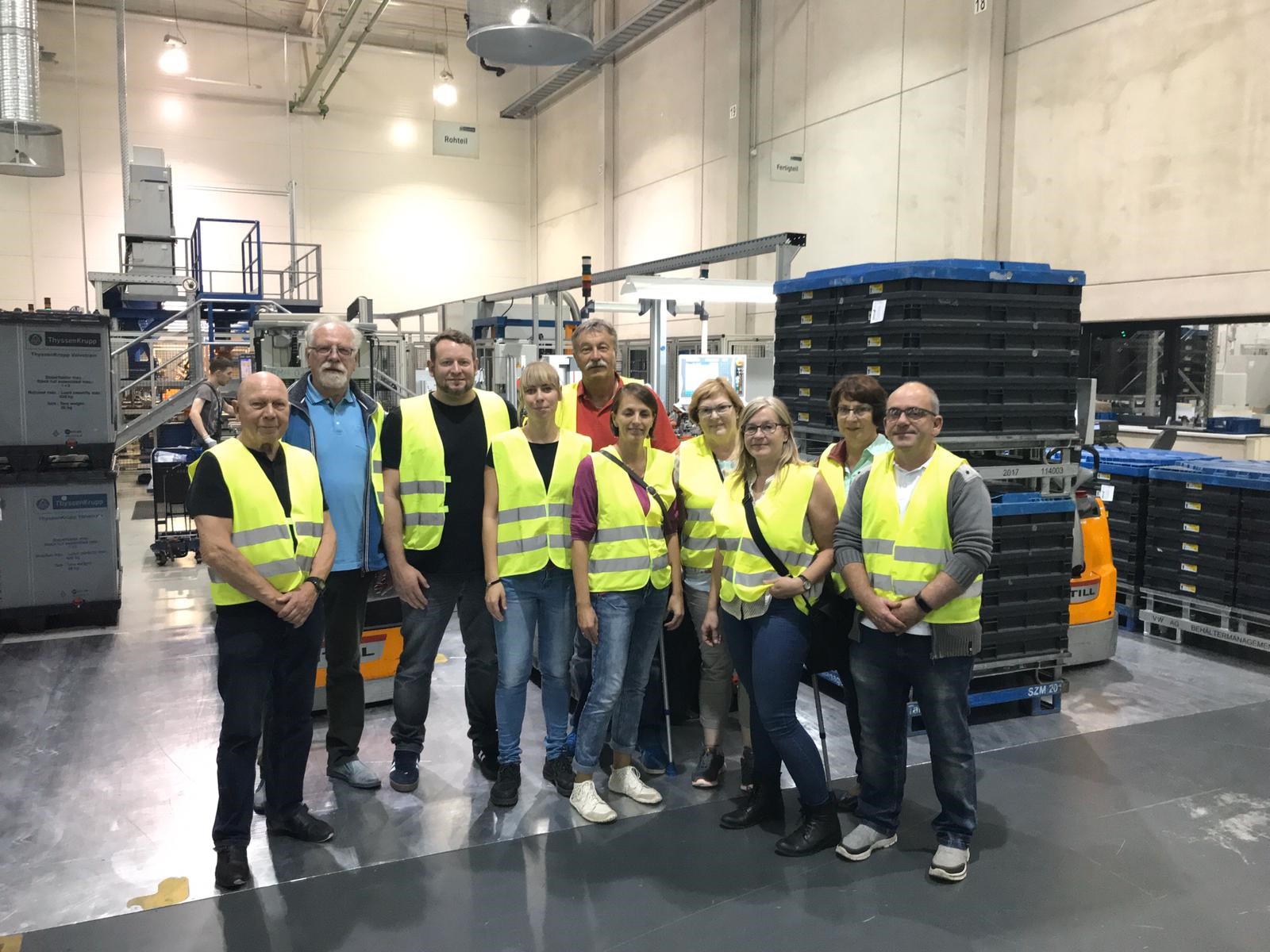10 Mitglieder mit gelben Westen in einer Produktionshalle