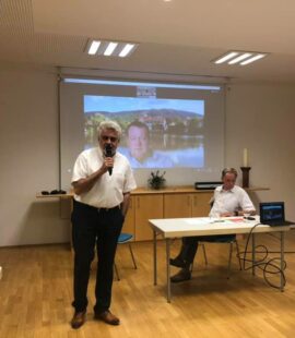 Armin Willingmann, grauhaarig, Anfang 60, steht mit einem Mikrofon vor einer Leinwand auf der Florian Fahrtmann zu sehen ist.