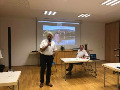 Armin Willingmann, grauhaarig, Anfang 60, steht mit einem Mikrofon vor einer Leinwand auf der Florian Fahrtmann zu sehen ist.