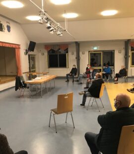 Viele Menschen sitzen in großem Abstand im Halbkreis vor einer Bühne, Florian Fahrtmann steht davor und referiert gerade