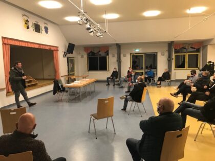 Viele Menschen sitzen in großem Abstand im Halbkreis vor einer Bühne, Florian Fahrtmann steht davor und referiert gerade