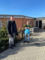 Florian Fahrtmann steht vor einem Altenwohnheim und eine Frau daneben mit zwei Blumensträußen