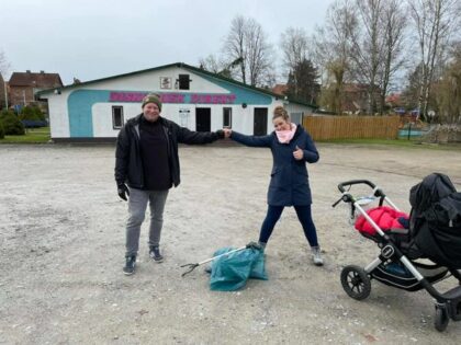 2 Personen stehen in großem Abstand vor einem mit Müll befüllten blauen Plastiksack
