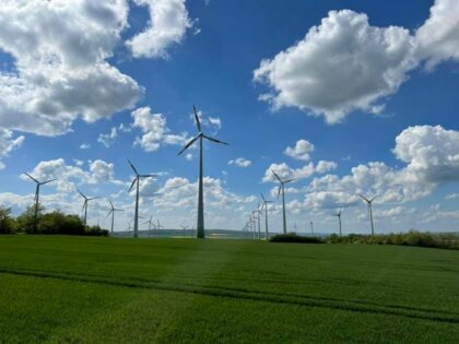 Windräder auf einer grünen Wiese mit blauem, leicht bedecktem Himmel