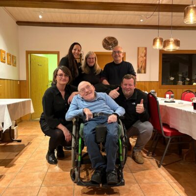 um einen Rollstuhlfahrer stehen mehrere Menschen und lächeln