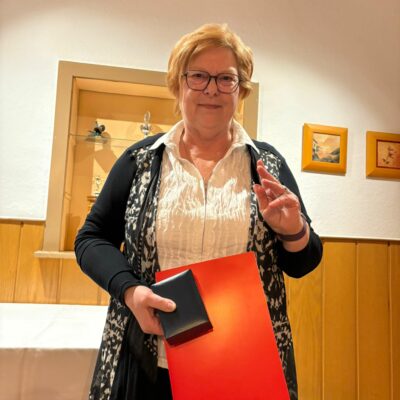 eine Frau Anfang 60 hält eine Urkunde in der Hand und freut sich